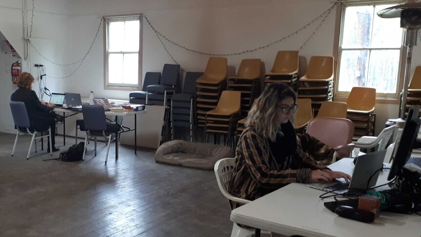 Two people at tables at far ends of  a hall, both working on computers