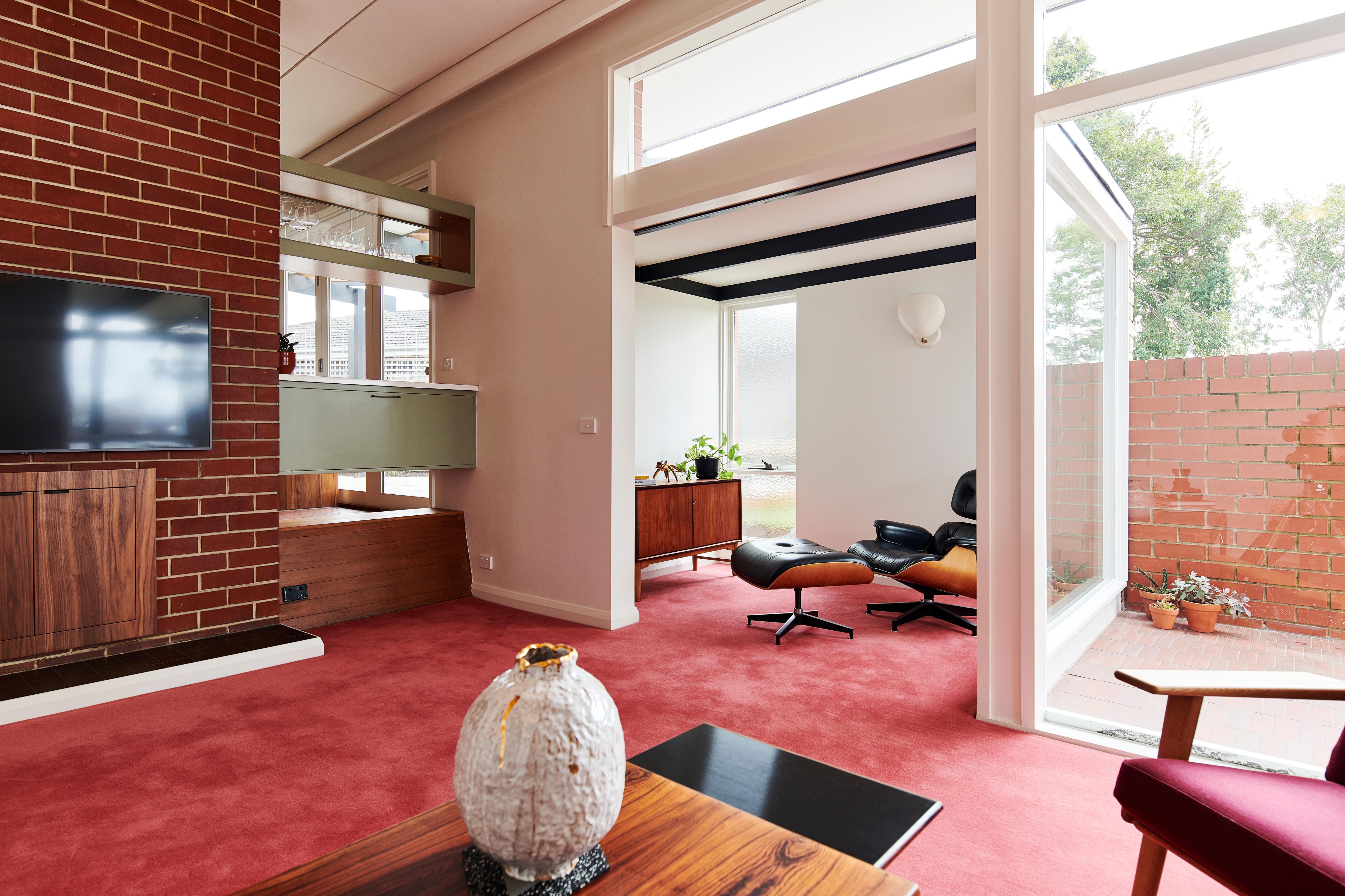 Современная гостиная в середине столетия с кирпичной стеной слева, офисным углом и большими окнами справа