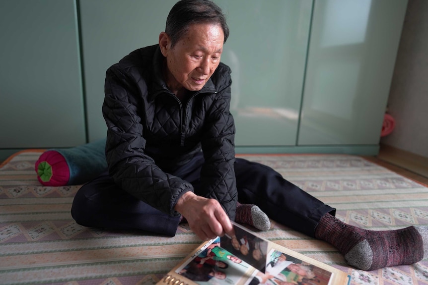 A man sits on the floor looking through a photo album.