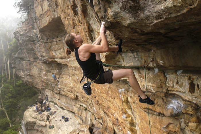  Libby Hall climbs a rock high above the ground.