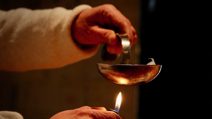 A hand holds a ladle and heats it with cigarette lighter.