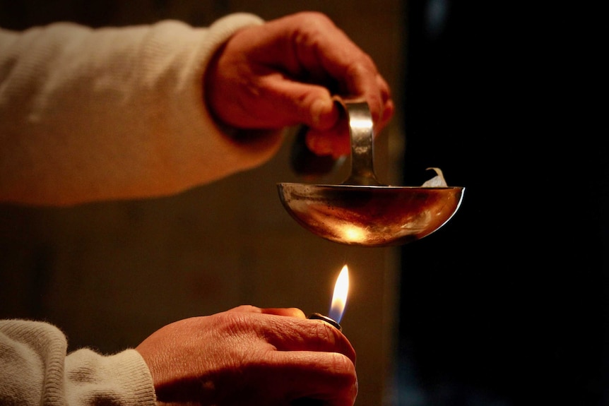 Hand holds ladle and heats it with cigarette lighter