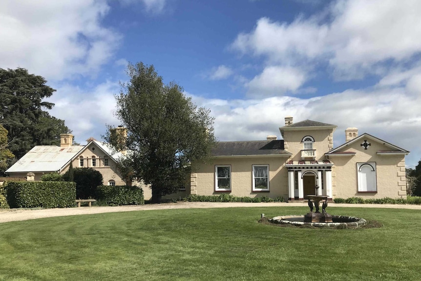 A very well kept historic home, painted in a beige colour.The lawns are perfectly manicured and there is a fountain