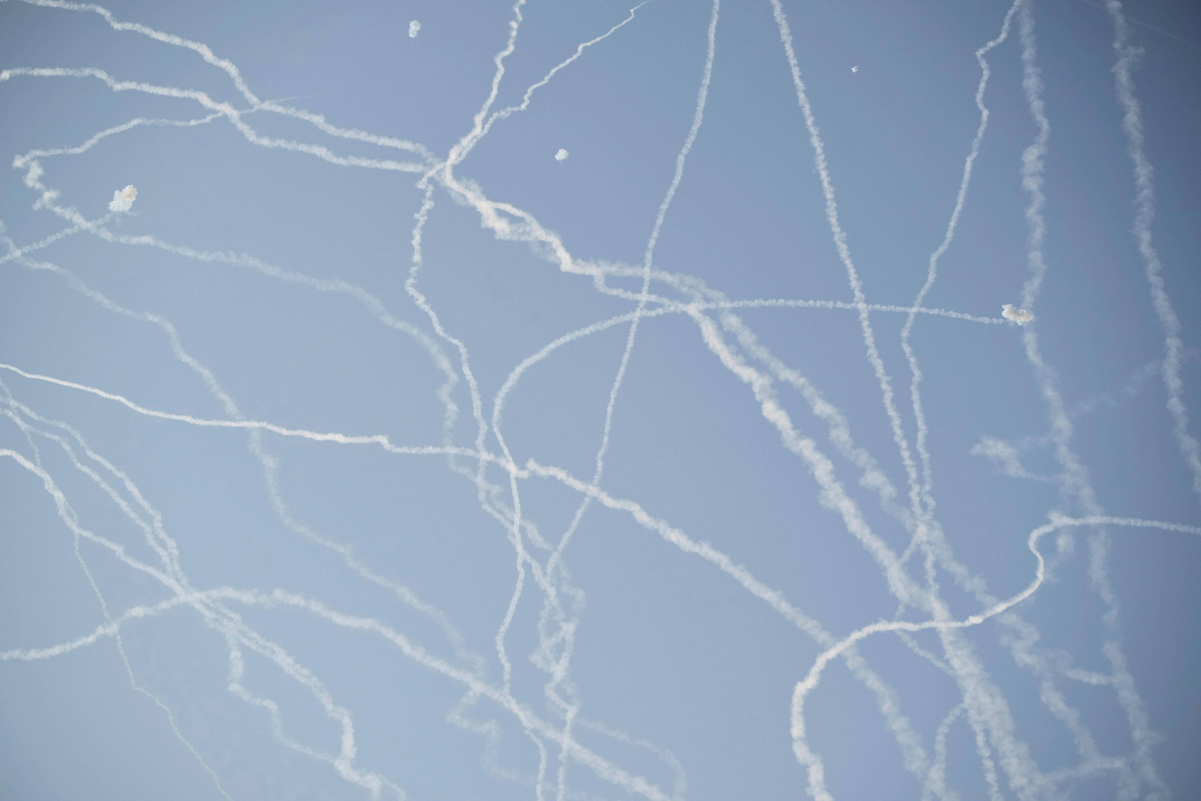 Smoking paths from multiple rockets go against a blue sky in many directions.