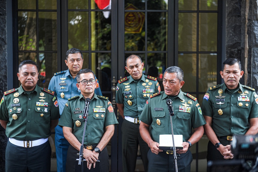 A uniformed Indonesian military commander speaks during a news conference with five fellow officers standing next to him.