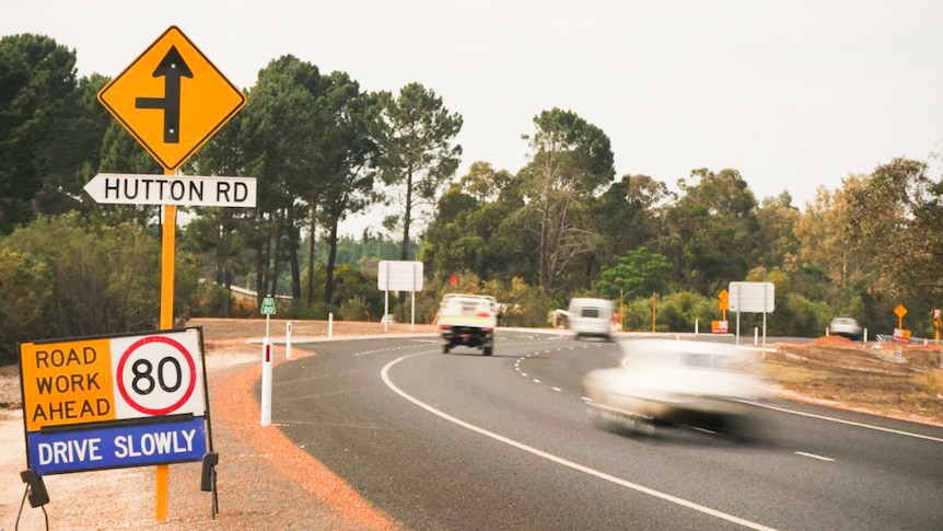 Two cars driving along a highway with a road works sign nearby 