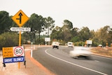 Two cars driving along a highway with a road works sign nearby 