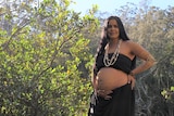 a pregnant Indigenous woman stands among trees