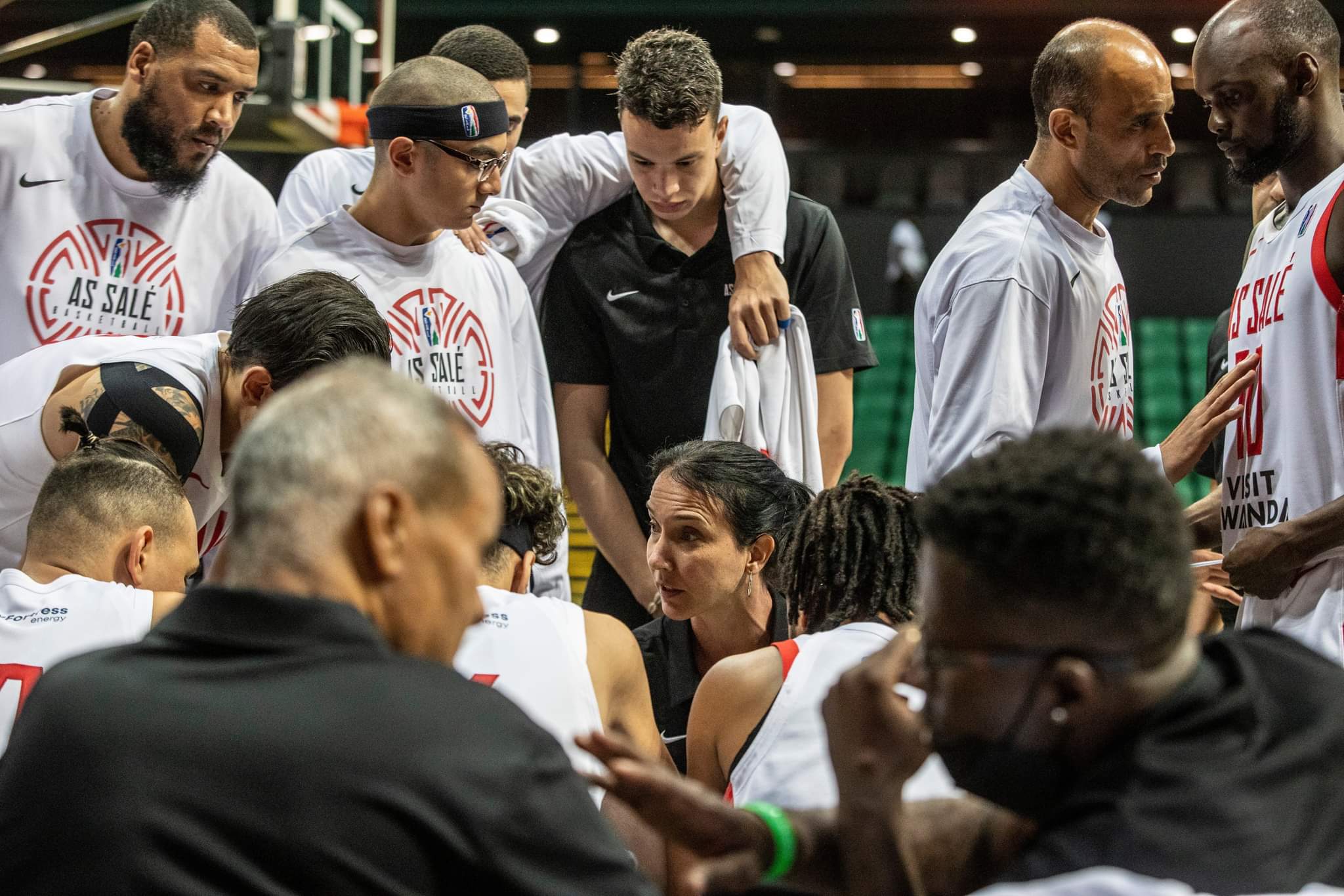 A woman head coach talks to her male basketball players during a game
