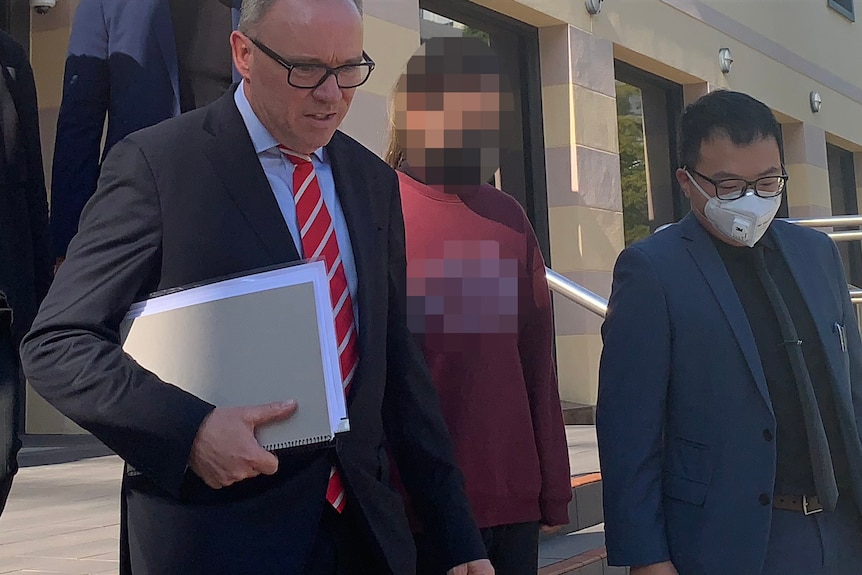 A girl with her face and jumper pixellated to disguise her identity walks out of court in Perth flanked by two lawyers.
