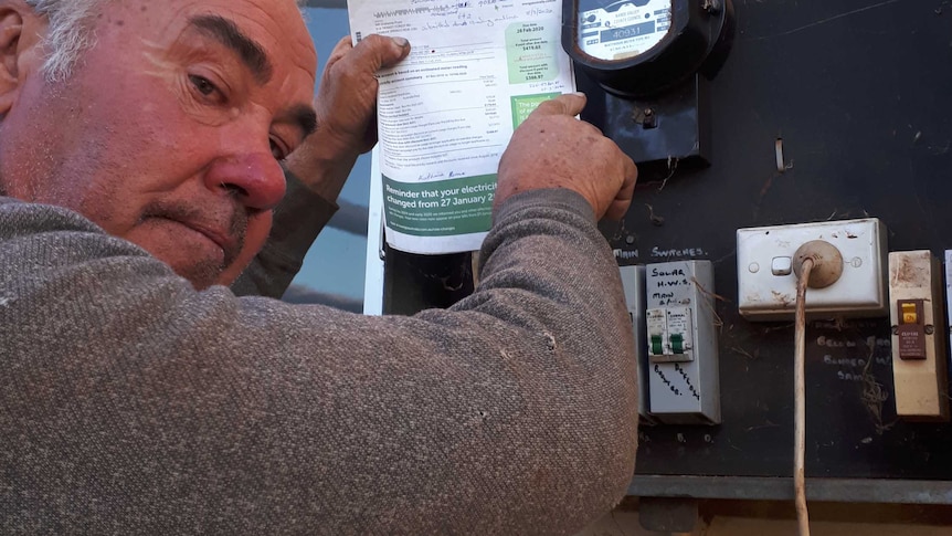 A man holding a power bill next to an electricity meter.