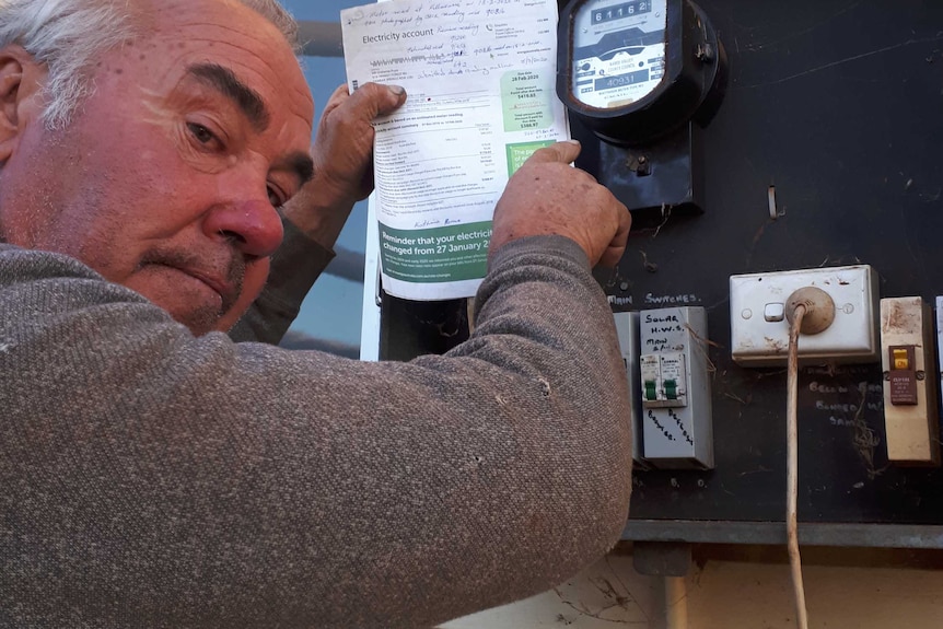 A man holding a power bill next to an electricity meter.