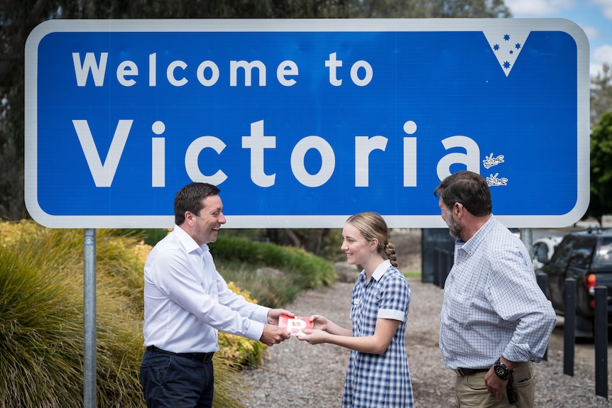 Matthew Guy stands in front of a blue sign reading 'Welcome to Victoria'.
