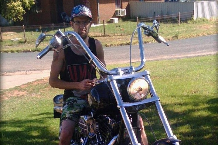 A man wearing a hat and glasses sits on a motorbike