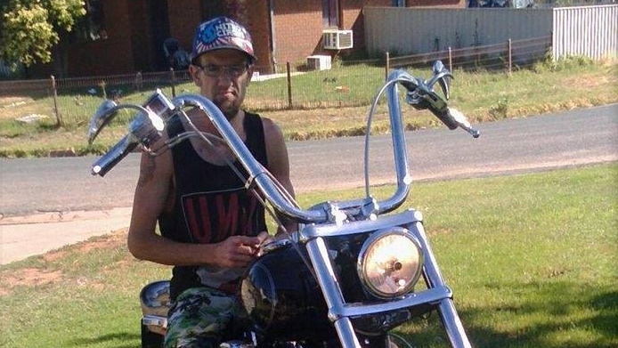 A man wearing a hat and glasses sits on a motorbike