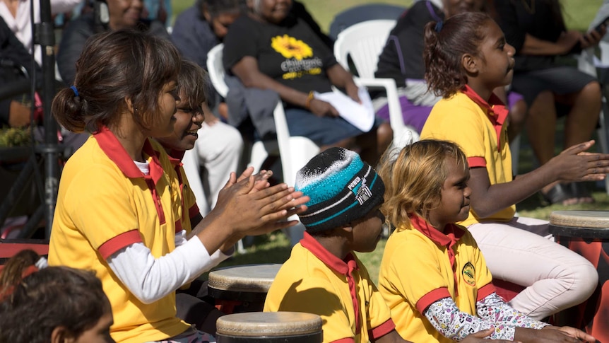 Children in yellow shirts clap and play the drums