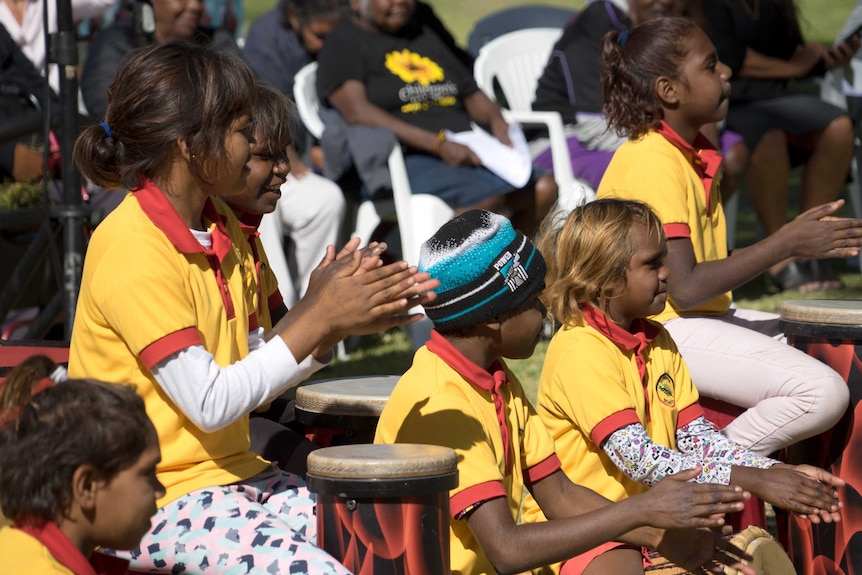 Children in yellow shirts clap and play the drums