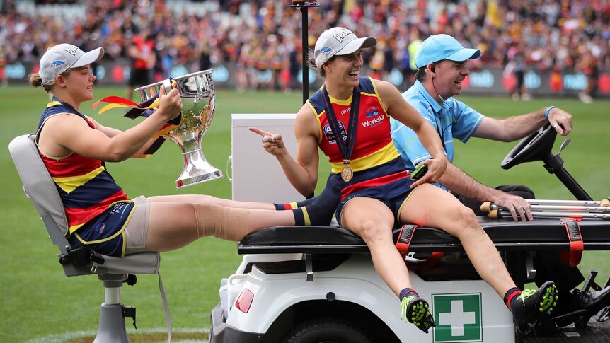 Chloe Scheer sits with her feet up on a medical vehicle holding the AFLW trophy