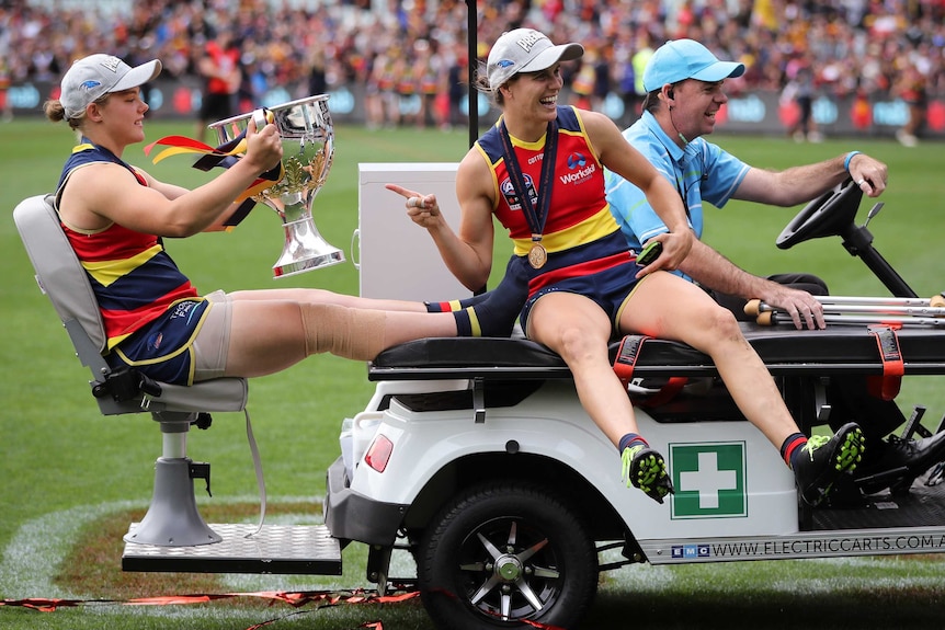 Chloe Scheer sits with her feet up on a medical vehicle holding the AFLW trophy