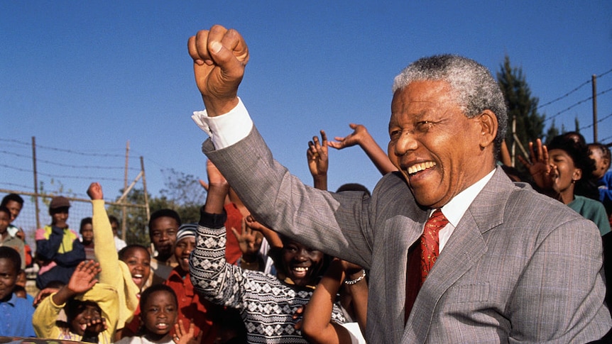 Nelson Mandela stands with fist in the air with an audience of school children in South Africa