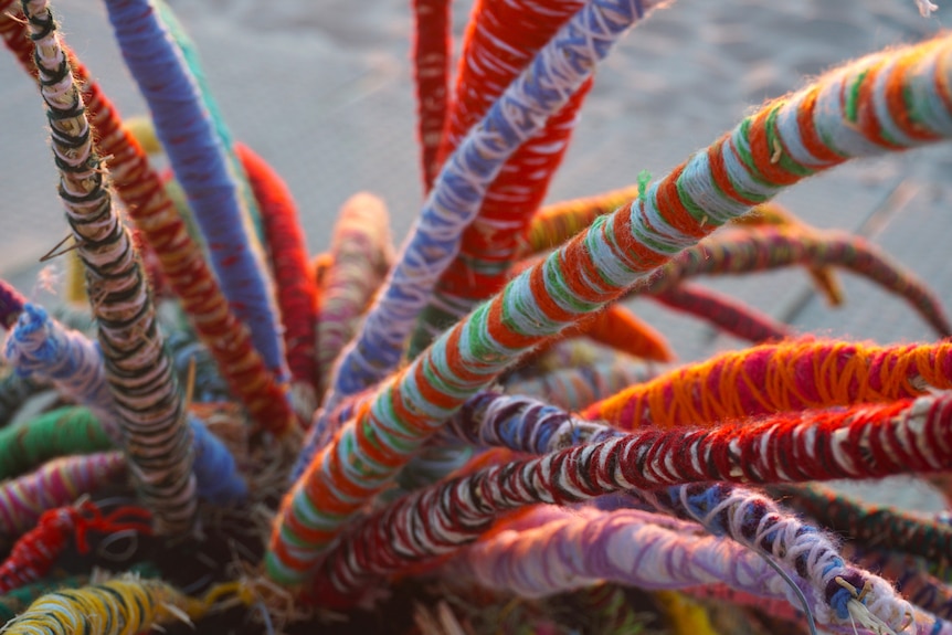 A detailed shot of sprigs of colourful yarn with sand in the background.