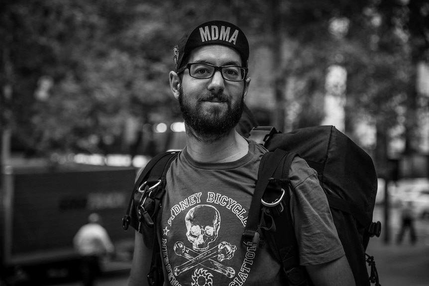 Black and white image of a man in a t shirt and cap, wearing a backpack