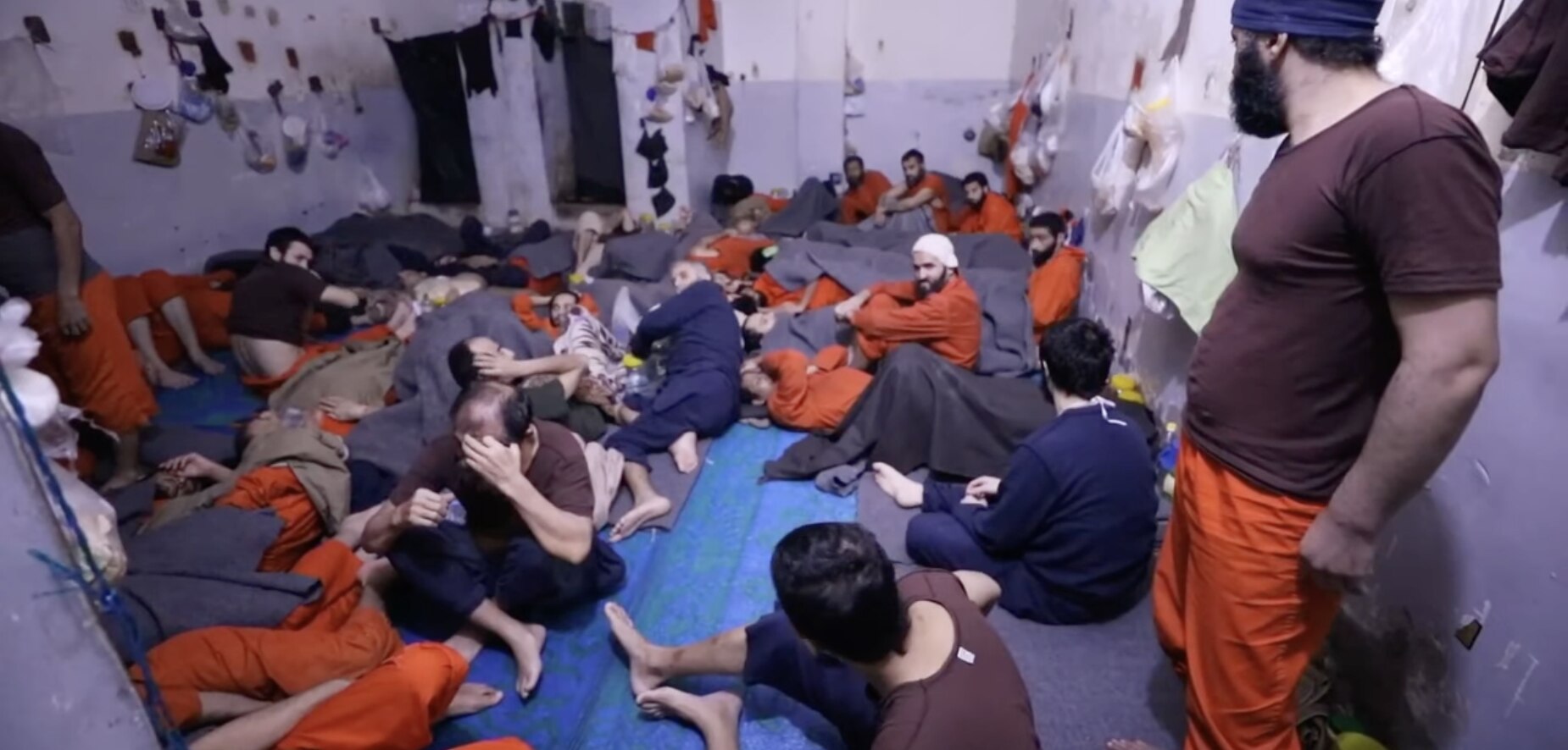 Men sit on the floor in a crowded prison cell in Syria