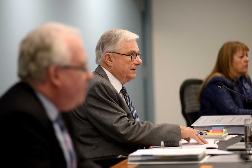 Peter McClellan and Helen Milroy with another man sitting at desk inside the Royal Commission.