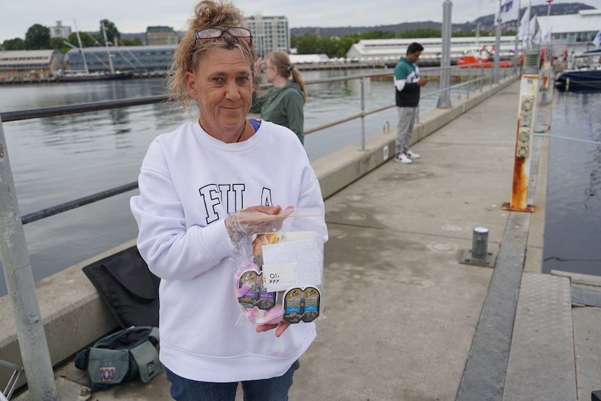 A woman holds up a clear bag with cat food inside it on a dock.