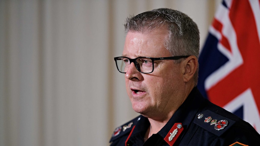 NT Police Commissioner Jamie Chalker is talking in front of a microphone. He looks serious.