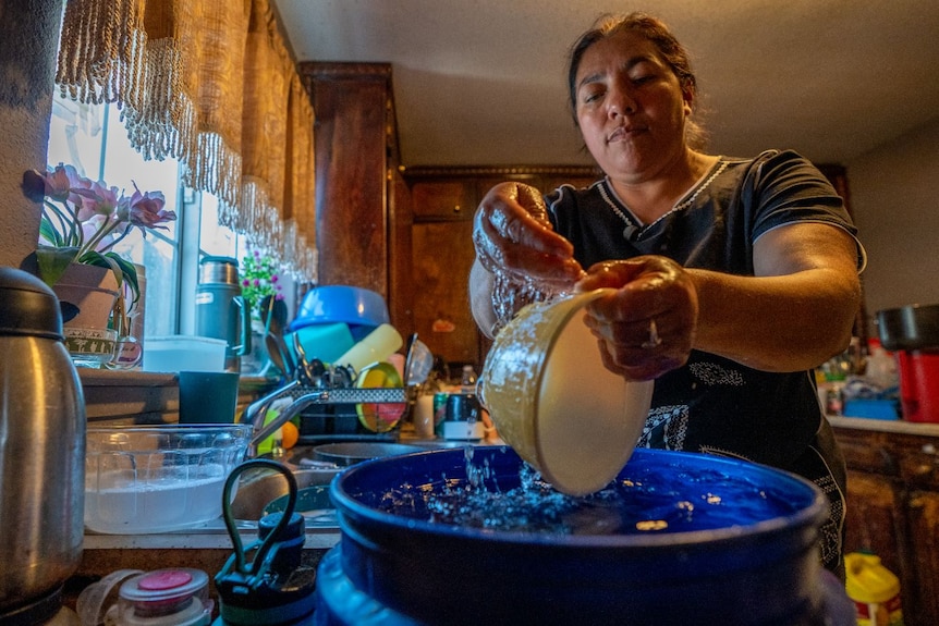 A woman washes a bowl in a bucket of water 