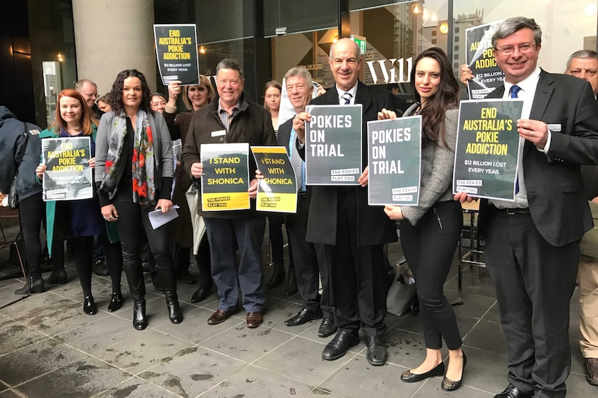 About a dozen supporters of the legal action hold up signs against the pokies.