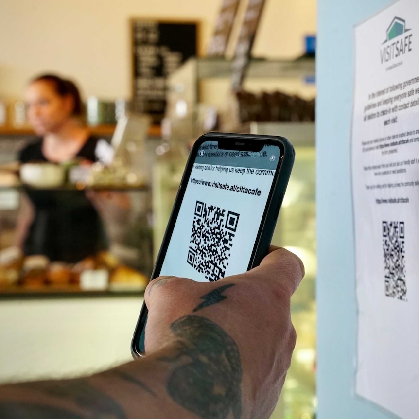 a tattooed hand holding a phone over a QR code in a cafe
