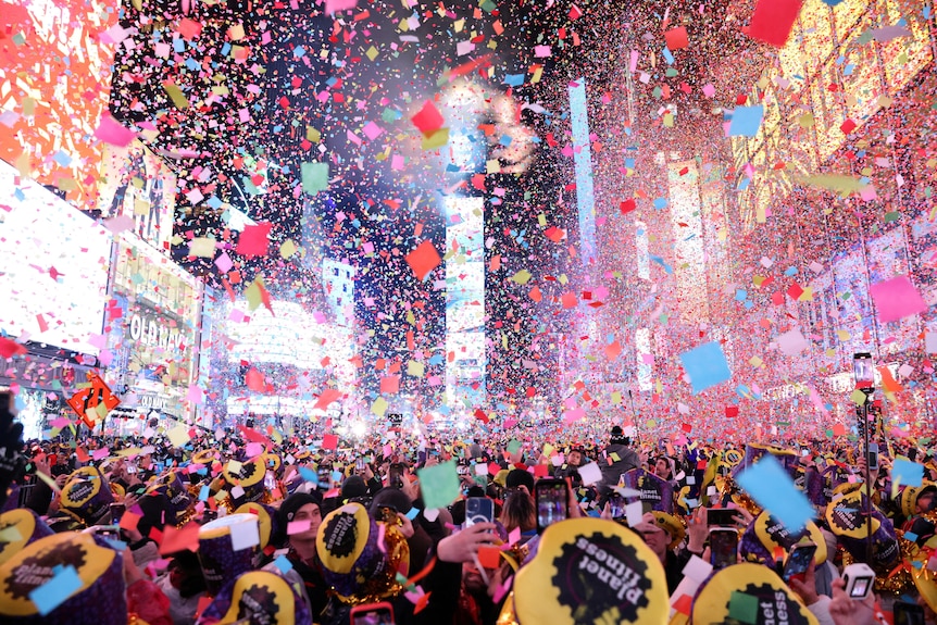 Confetti fills the air above a cloud of people in a square surrounded by bright advertising signs.