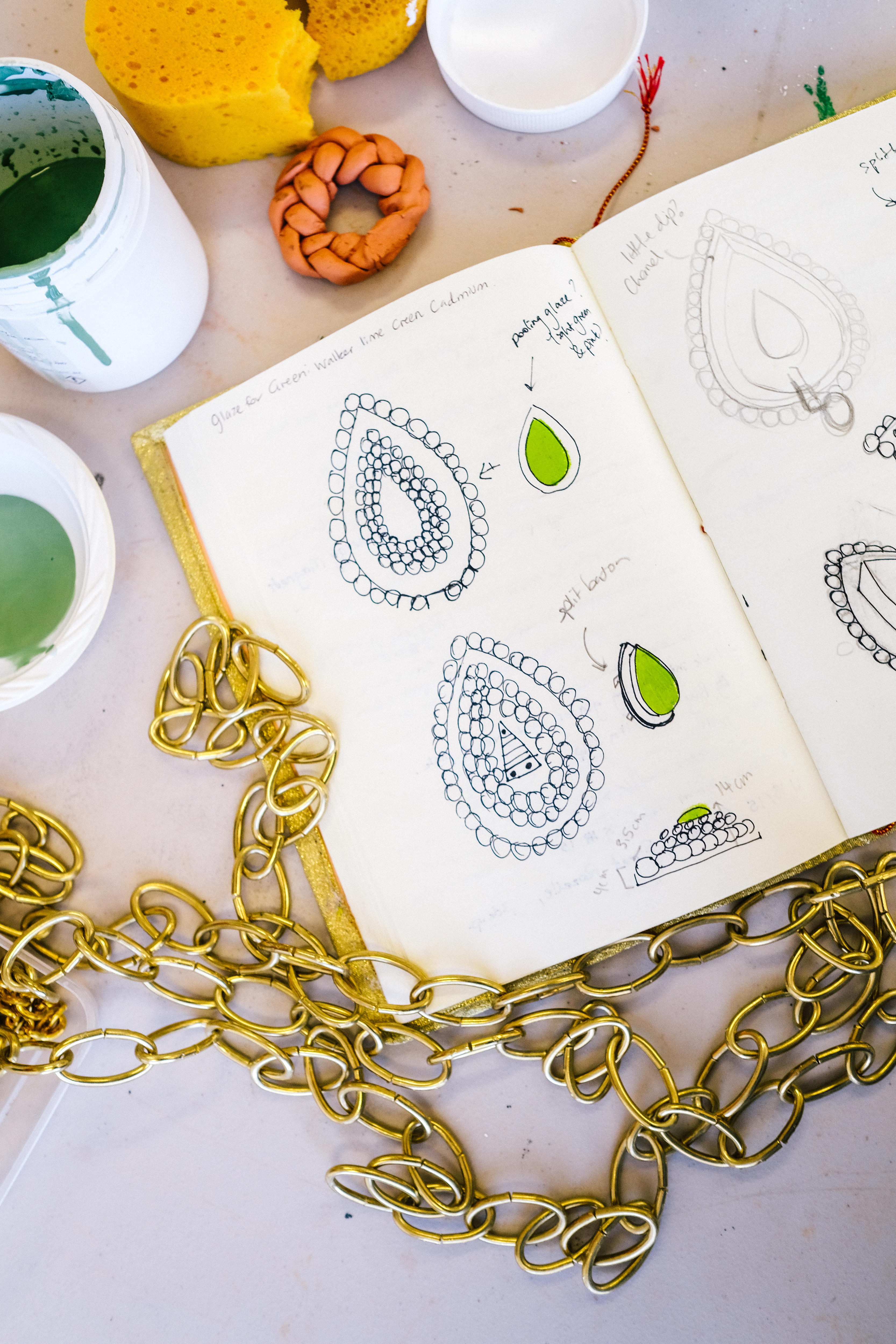 Close up and overhead images of a sketchbook with drawings of earrings, and gold chain.