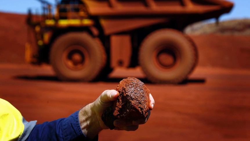 A man holds a piece of iron ore in front of a remote-controlled truck in Sheila Valley, WA.