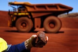 A man holds a piece of iron ore in front of a remote-controlled truck in Sheila Valley, WA.