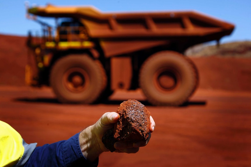 Un hombre sostiene un trozo de mineral de hierro frente a un camión controlado remotamente en Sheila Valley, WA.