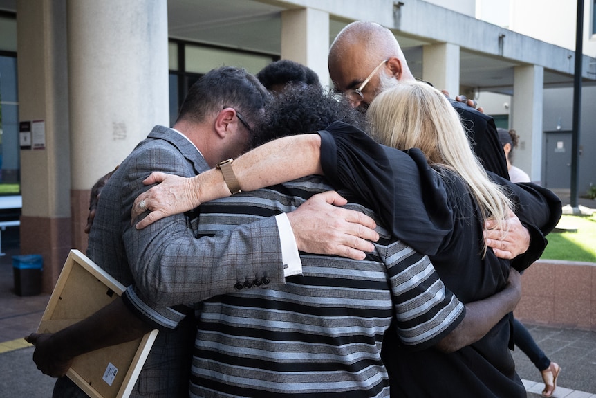 A group embrace of five people outside of courthouse 