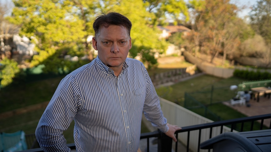 A man stands on a balcony with a frown on his face.