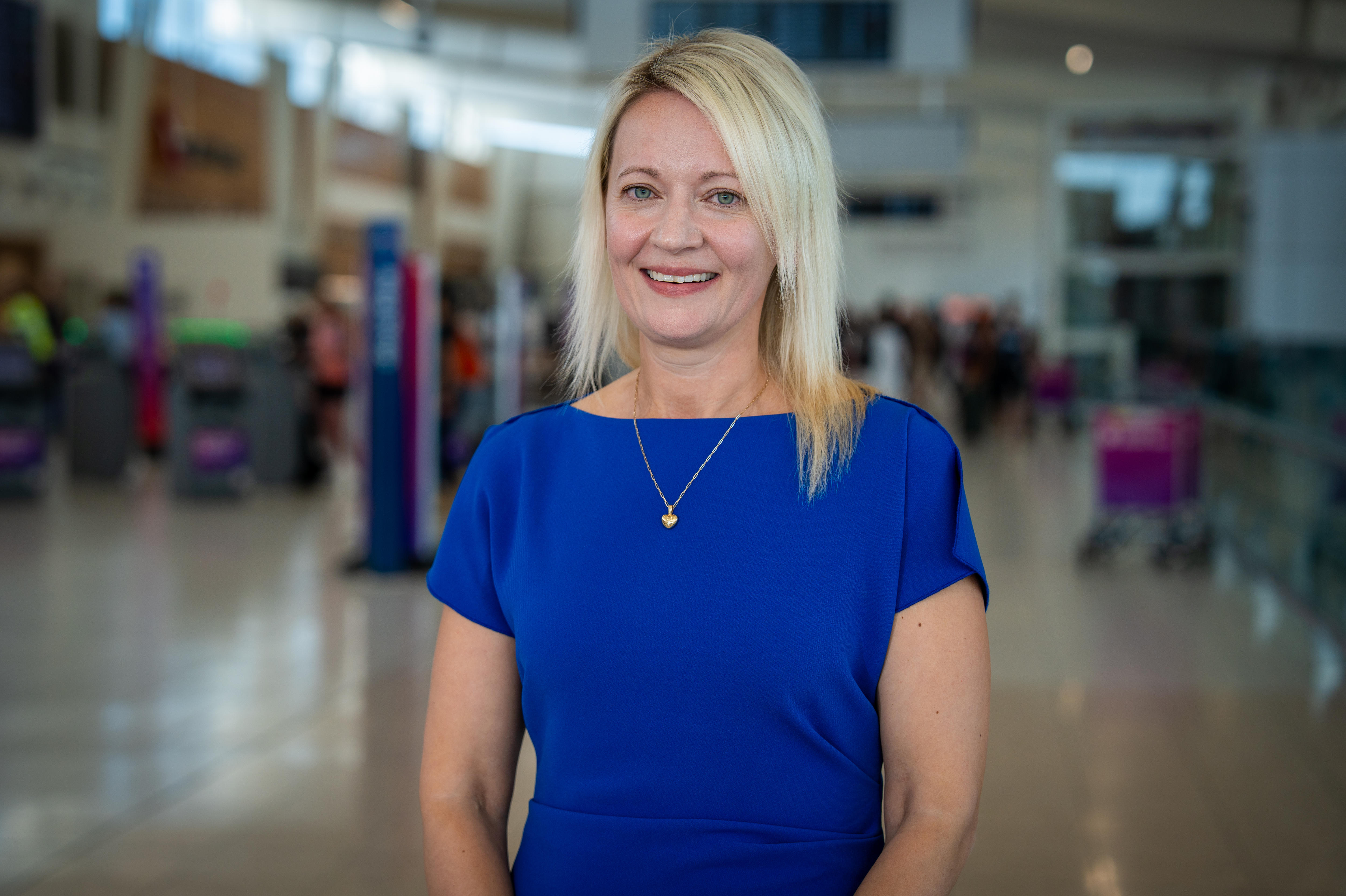 Una mujer de cabello rubio con un vestido azul en un aeropuerto.