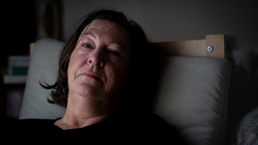 A middle-aged white woman lying in bed looking exhausted