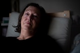 A middle-aged white woman lying in bed looking exhausted