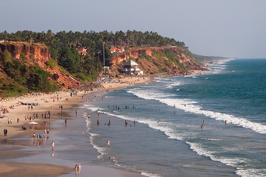 A wide view shows cliffs and people enjoying Varkala Beach in Kerala.