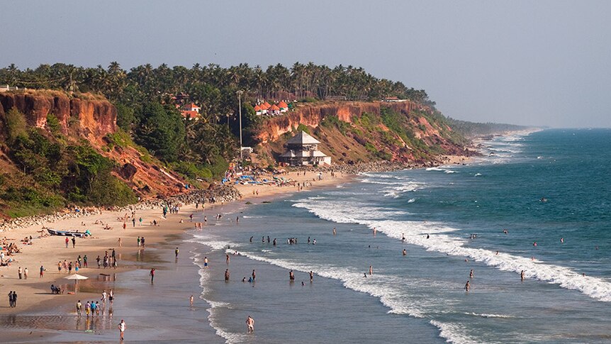 A wide view shows cliffs and people enjoying Varkala Beach in Kerala.