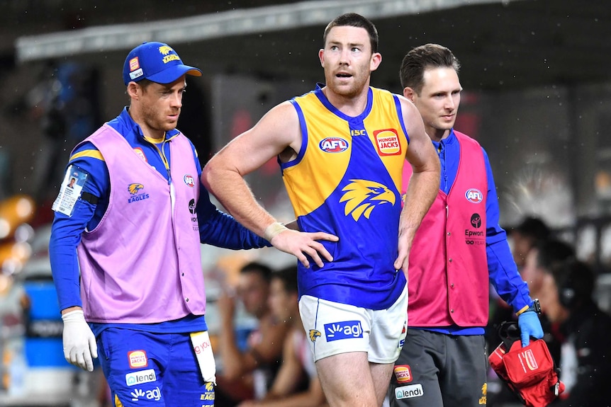 A West Coast Eagles AFL player walks off the field between two of the club's medical staff.