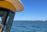 The cab of a marine search boat takes up the left third of the shot with the ocean in the background and small boats