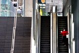 A women wearing a masks walks down an escalator in an empty streetscape.