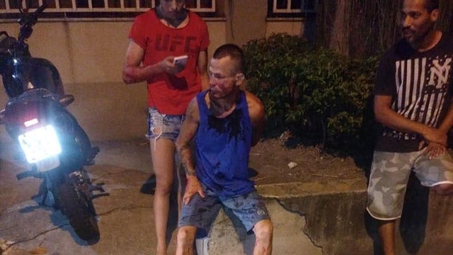 A man sits on the sidewalk held down by a UFC fighter after an attempted mugging in Rio de Janeiro