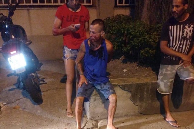 A man sits on the sidewalk held down by a UFC fighter after an attempted mugging in Rio de Janeiro